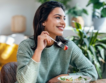 Woman in green sweater eating salad at home