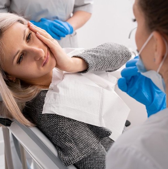 Woman sitting in the patient’s chair holding her jaw