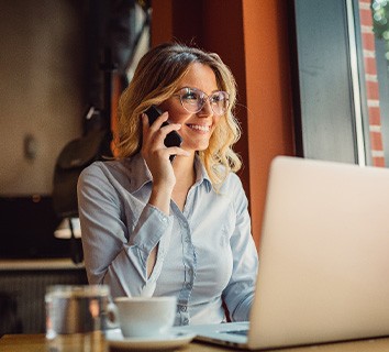 Woman smiling while talking on phone and working on laptop