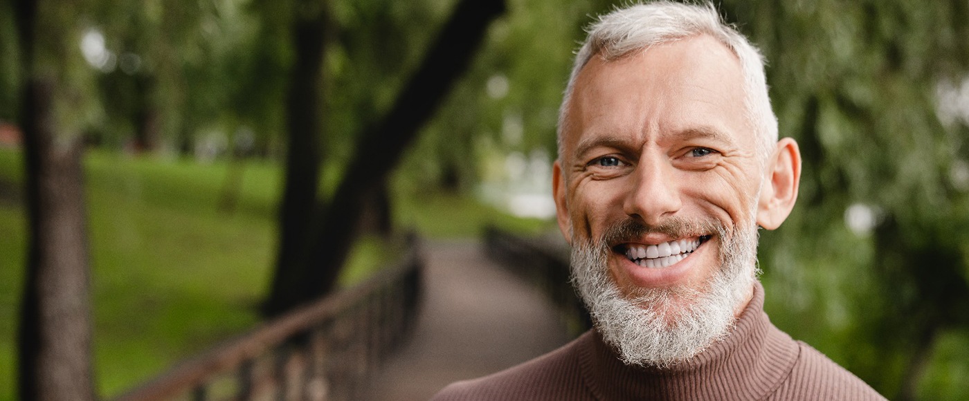 Man in brown sweater standing on a bridge and smiling