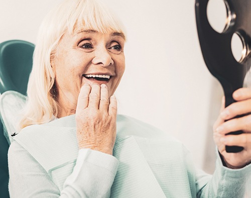 An elderly woman admiring her dentures in a hand mirror