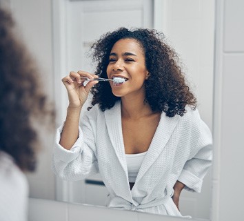 Woman smiling while brushing her teeth in bathroom