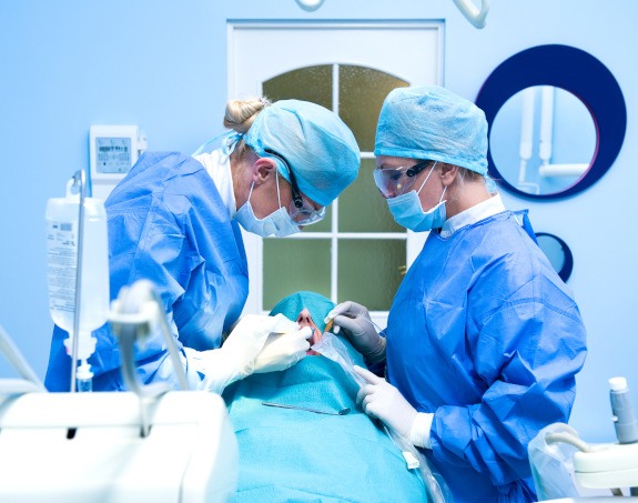 Two dentists in blue scrubs on either side of a patient under sedation