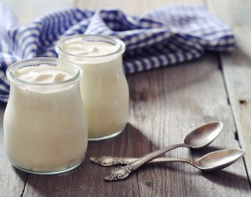 Two glass jars of yogurt with two spoons on a wooden table