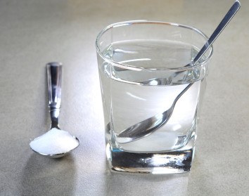 A spoon of salt next to a glass of water with another spoon