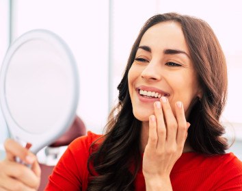 Woman in red shirt smiling at her reflection in hand mirror