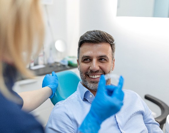 Patient smiling while placing clear aligner on top teeth