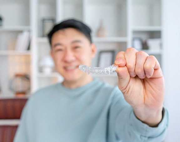 Man smiling while holding Invisalign aligner