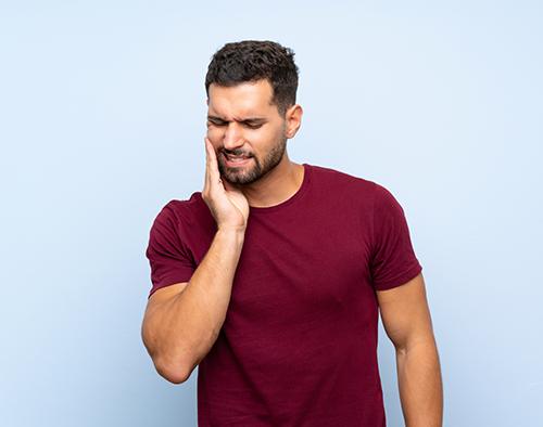 Man in burgundy t-shirt experiencing dental pain